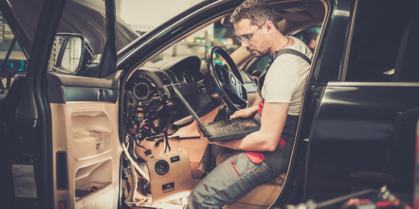 Mechanic sitting in vehicle with laptop