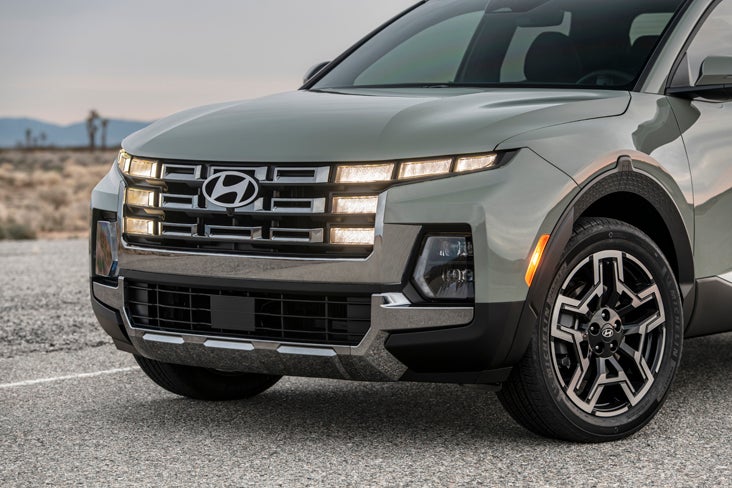 A Hyundai service technician in a grey and navy uniform uses a pneumatic impact wrench on a car tire in a professional garage.