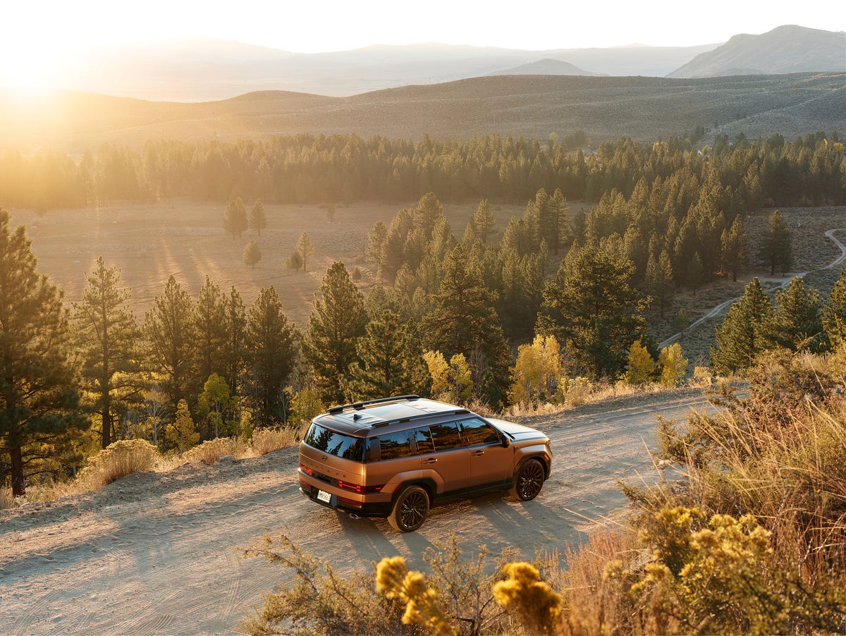 A brown new Hyundai Santa Fe Hybrid in Phoenix drives away from the viewer to the right seen from a high angle on a gravel road on the side of a rural mountain.
