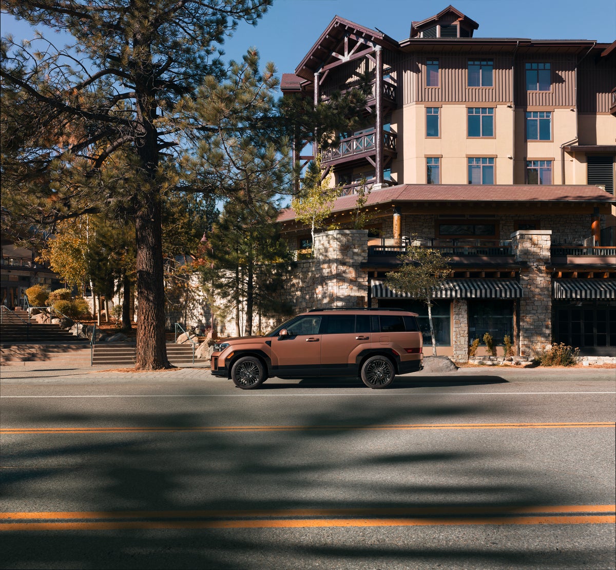 A brown new 2026 Hyundai Hybrid SUV in Phoenix drives to the left on a city street.